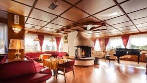 Un salon spacieux doté d’une cheminée, de canapés, d’un piano à queue et d’un parquet en bois.