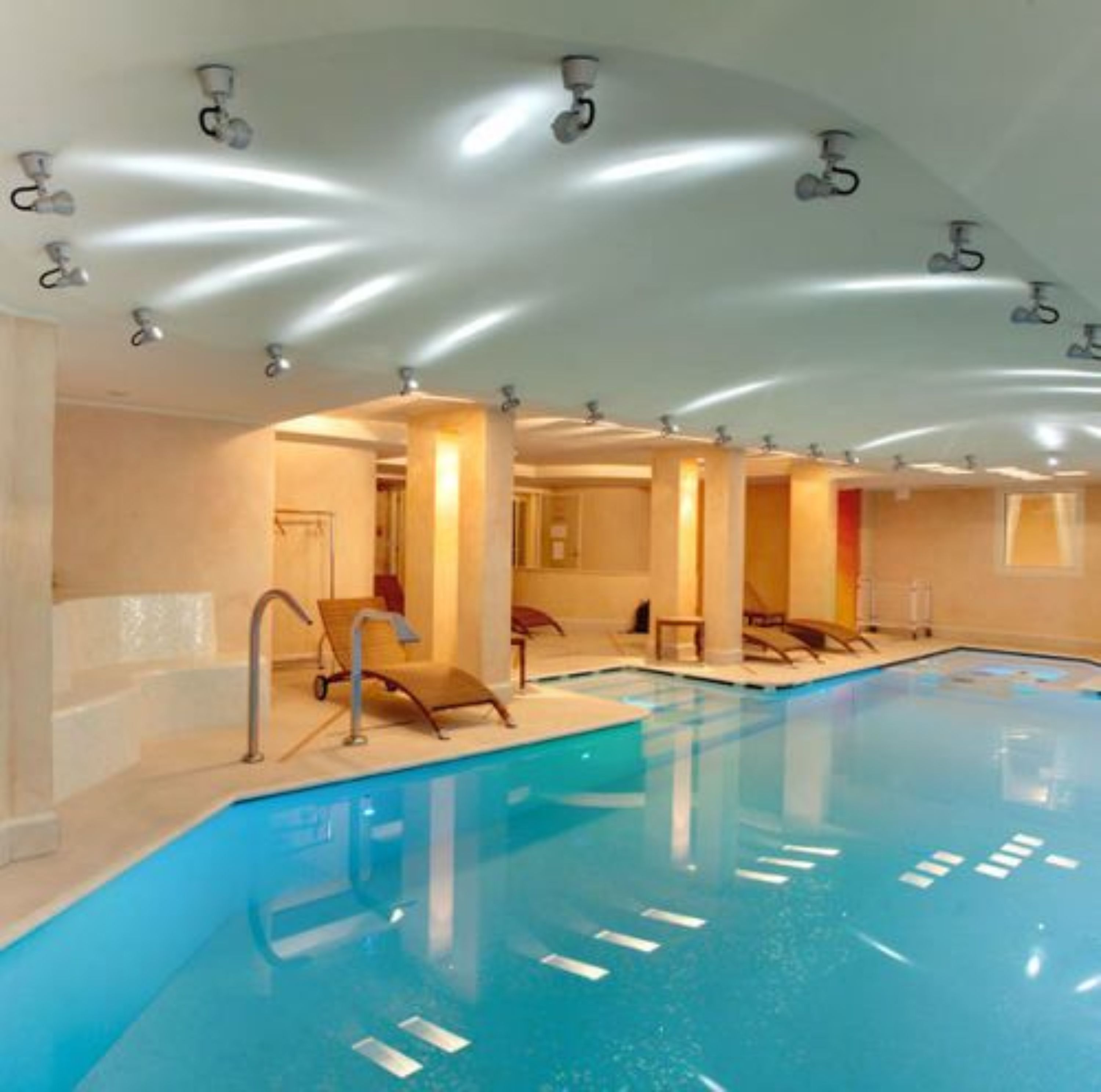 Una piscina al coperto con diverse corsie, luci a soffitto e poltrone relax.