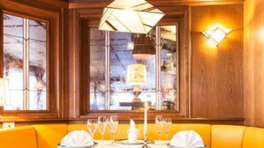 Une table à manger dressée avec une nappe blanche, des bougies et des verres, entourée de sièges rembourrés de couleur jaune.
