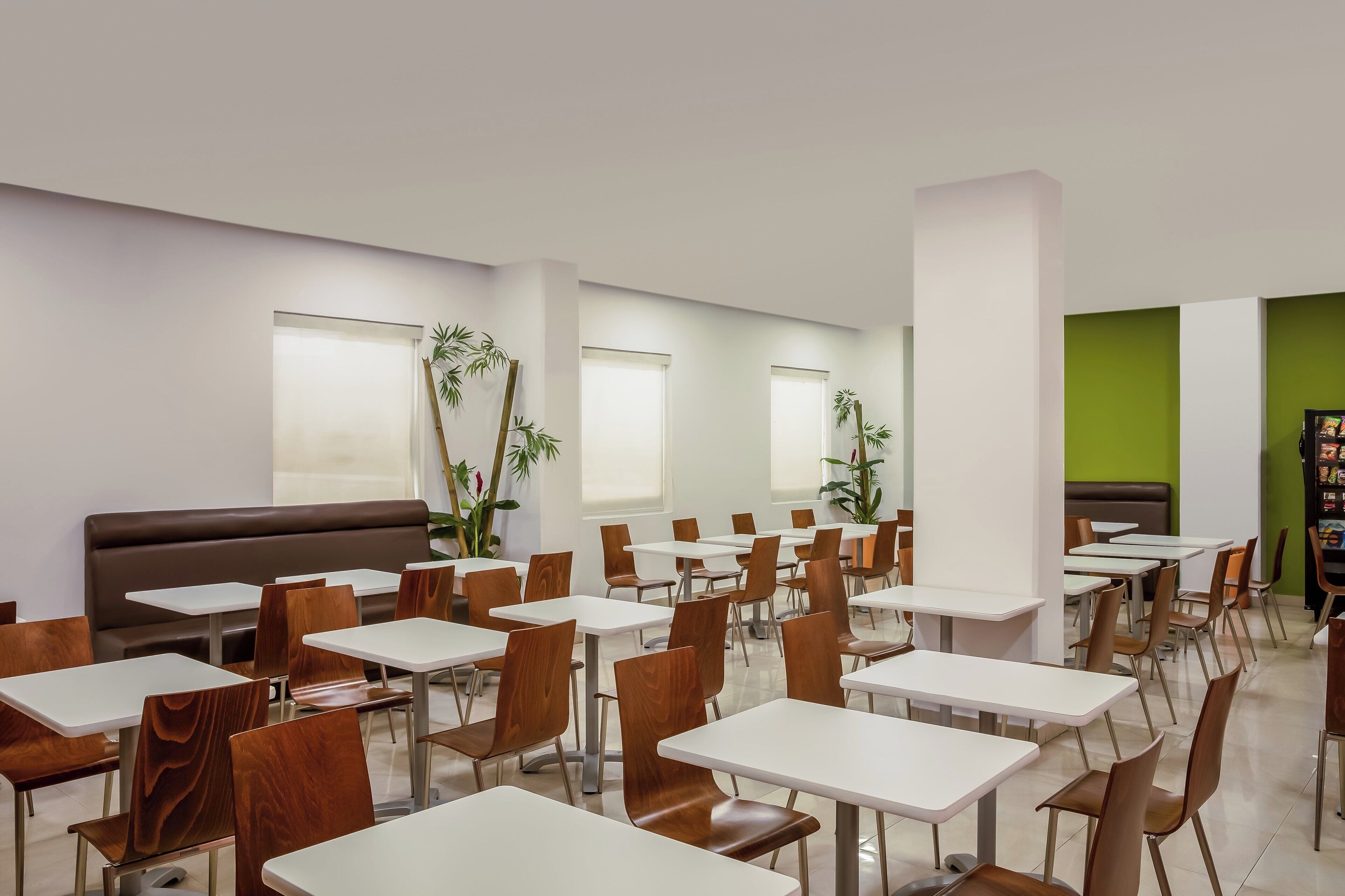 A modern dining area with white tables and brown chairs, a brown booth, and green walls.