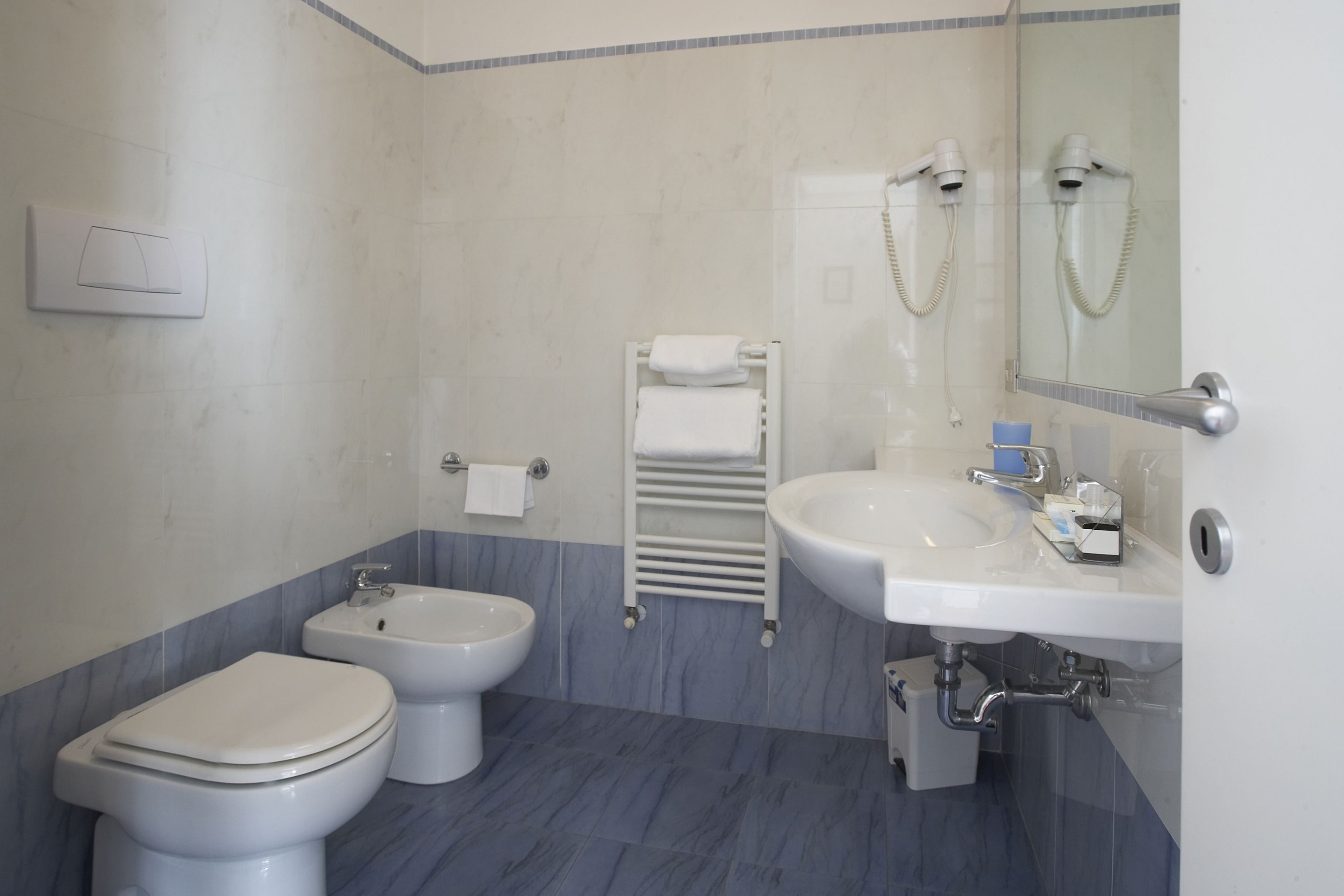 A bathroom with a toilet, bidet, and sink, with a towel rack and a mirror.
