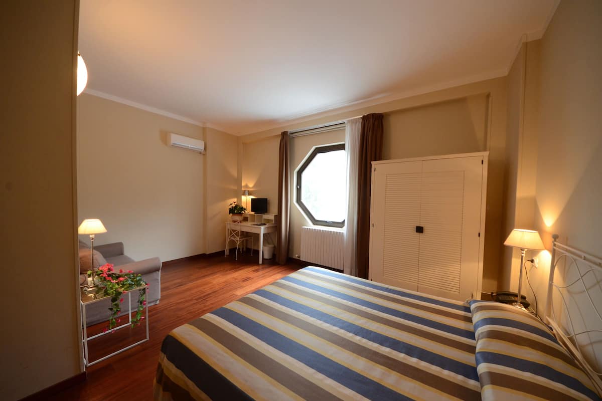 Una habitación de hotel con cama, escritorio, silla, ventana y radiador.