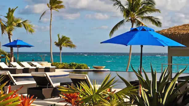 A resort pool area with lounge chairs and blue umbrellas, overlooking a turquoise sea. - Sky Beach Club (Governor's Harbour)