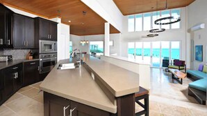 A spacious kitchen with dark cabinets, a large island, and a view to the living area. - Sky Beach Club (Governor's Harbour)