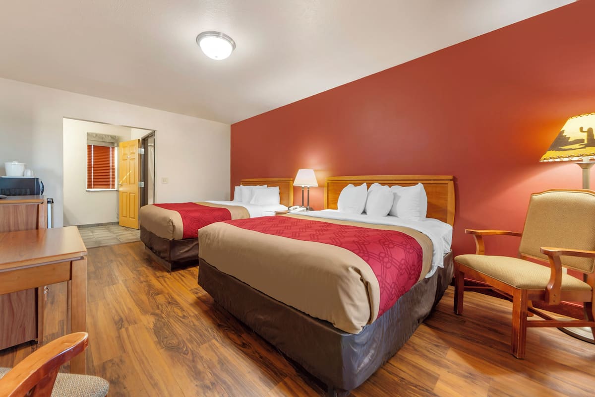 A hotel room with two beds, a desk, a chair, and a lamp.