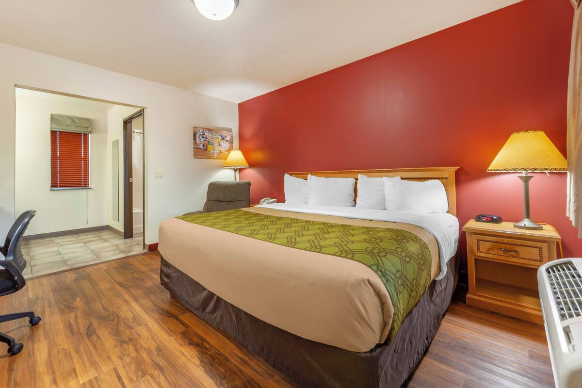 A hotel room with a bed, bedside lamps, a wooden nightstand, a chair, and a desk with a lamp.