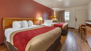 A hotel room with two beds, wooden headboards, a desk, and a chair.
