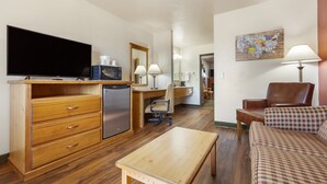 A compact hotel room with a wooden desk, a television, a microwave, a sofa, and a dining table.