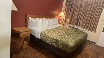 Une chambre d’hôtel avec un lit en bois, un bureau, une chaise, une lampe et une fenêtre avec des rideaux.