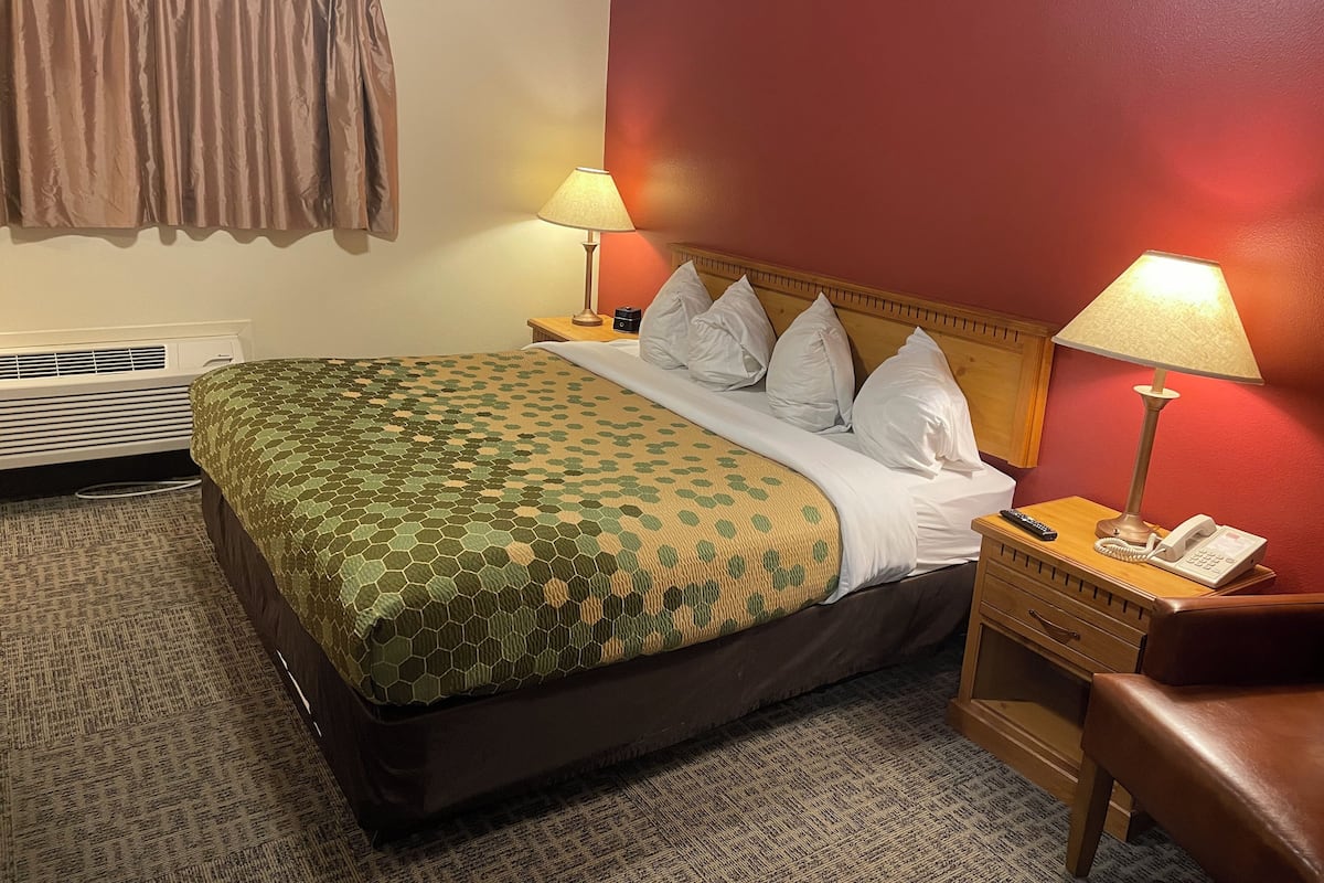 A hotel room with a bed, two bedside lamps, a telephone, a wooden nightstand, and a red wall.