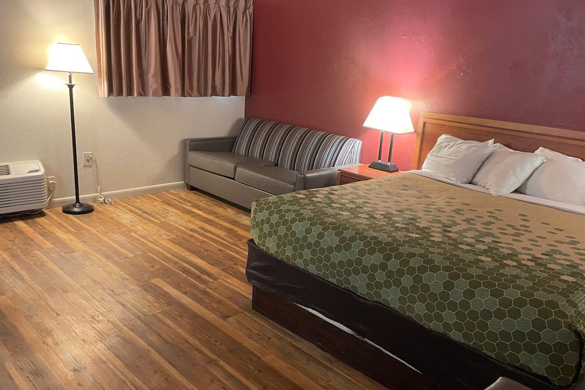A hotel room with a bed, a sofa, two lamps, and an air conditioning unit.