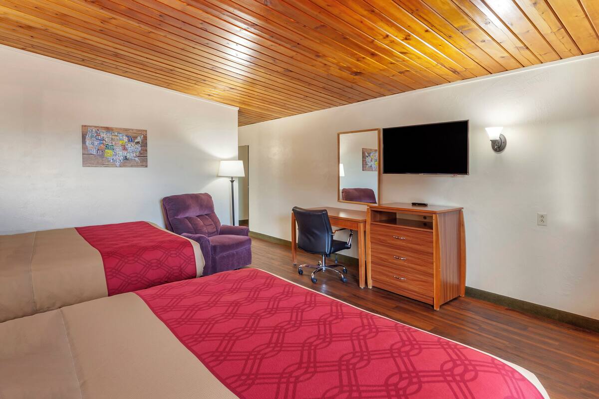 A hotel room with two beds, a desk, a chair, a TV, and a map on the wall.