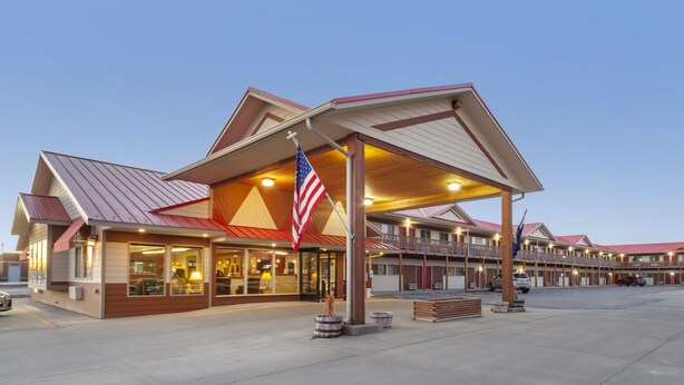 A motel with a red roof, American flag, and a covered parking area.