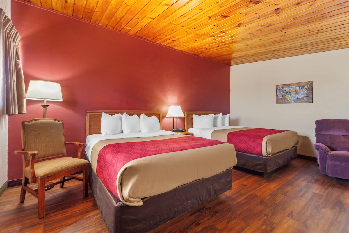 A hotel room with two beds, wooden flooring, a wooden ceiling, and a red wall.