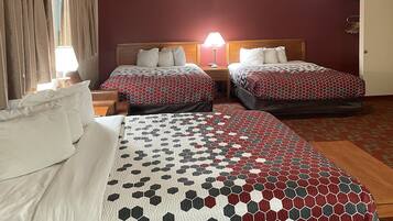 A hotel room with two beds, each with a patterned bedspread, a nightstand with a lamp, and a wooden headboard.