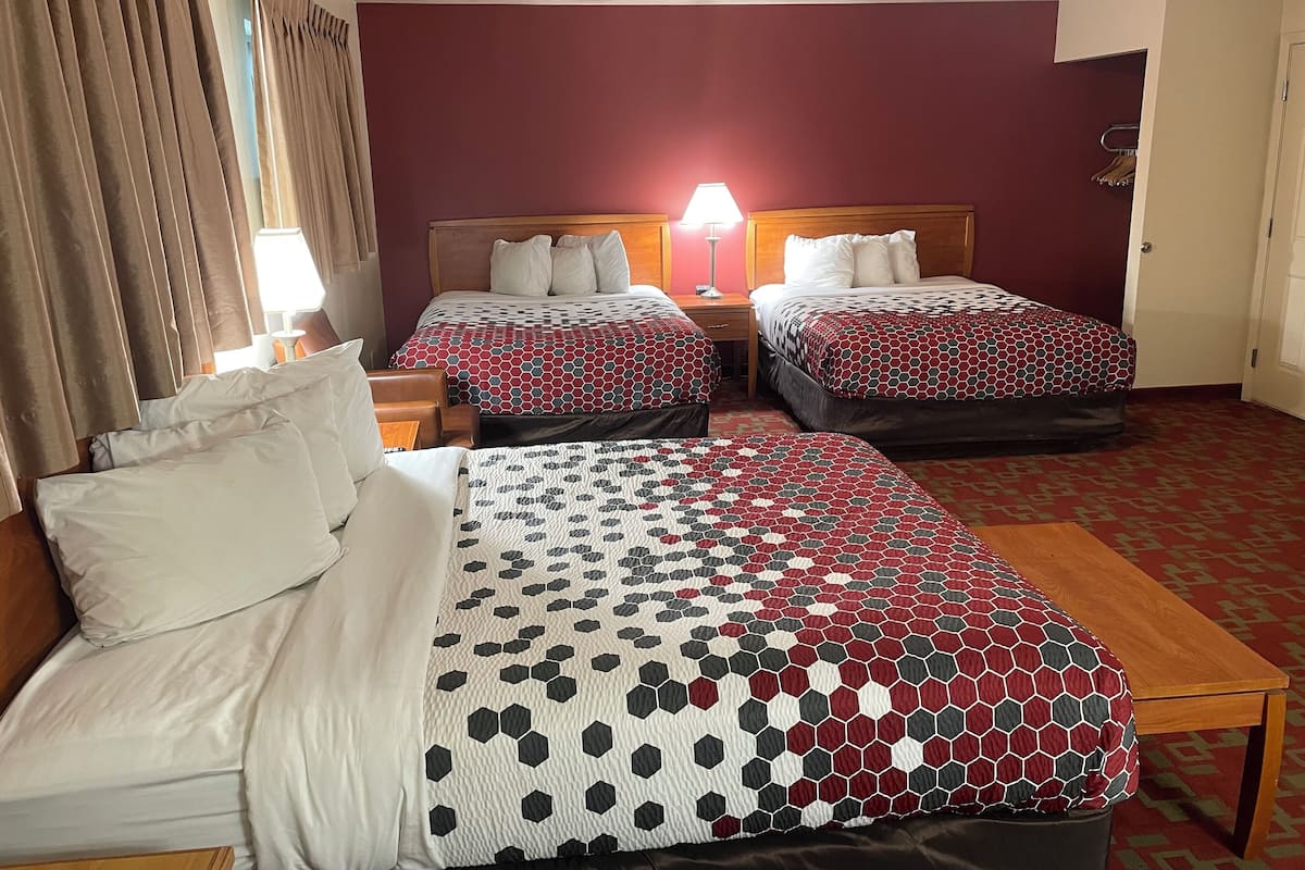 A hotel room with two beds, a wooden nightstand, a lamp, and a red carpeted floor.