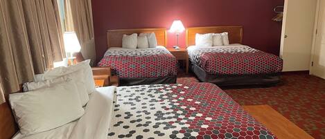 Habitación de hotel con dos camas, una mesita de noche de madera, una lámpara y suelo cubierto de alfombra roja.
