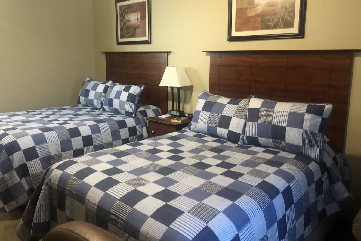 A hotel room with two beds, each with a checkered bedspread, a wooden headboard, a nightstand with a lamp, and two framed pictures on the wall.