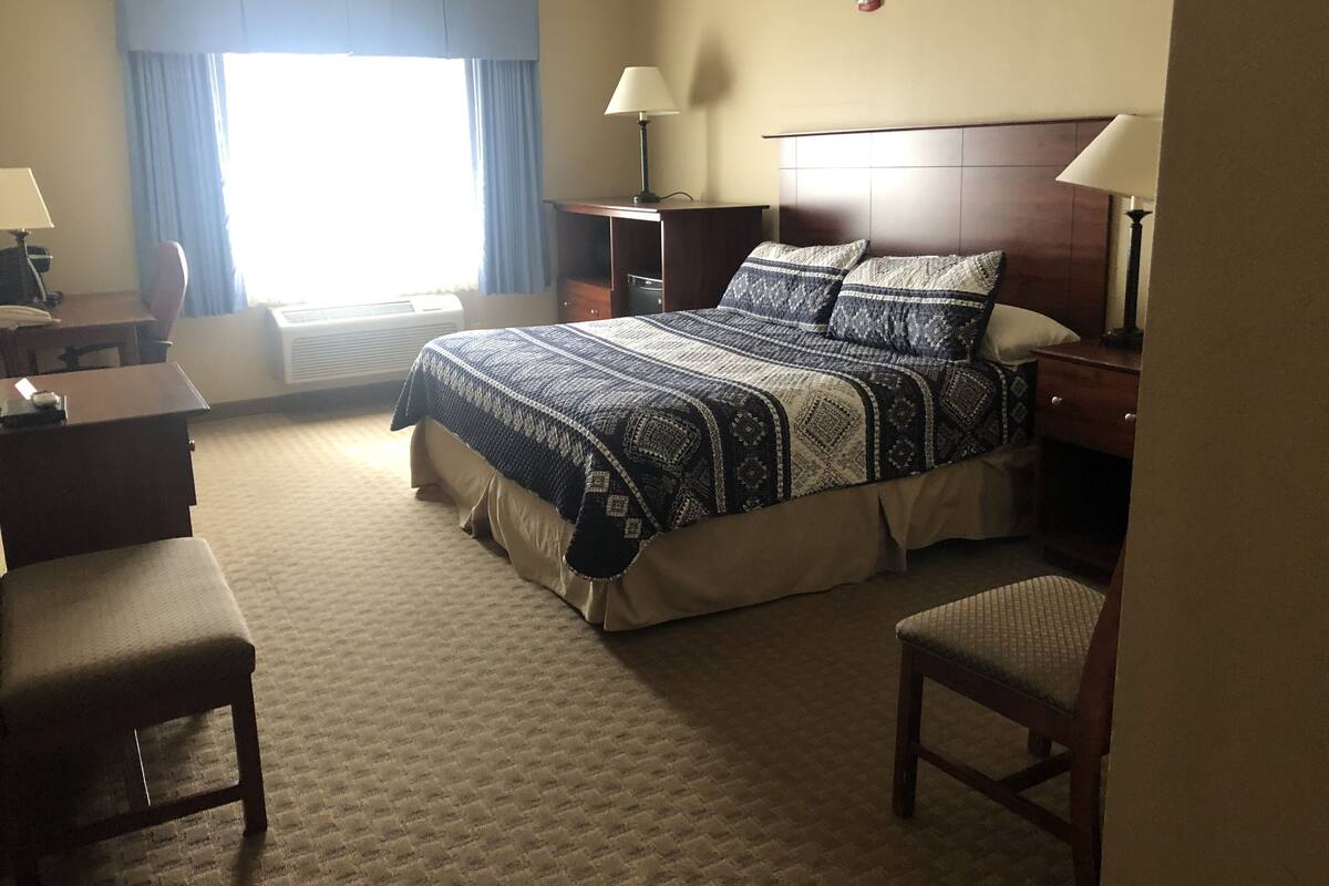 A hotel room with a bed, two bedside tables, a desk, a chair, and a window with curtains.