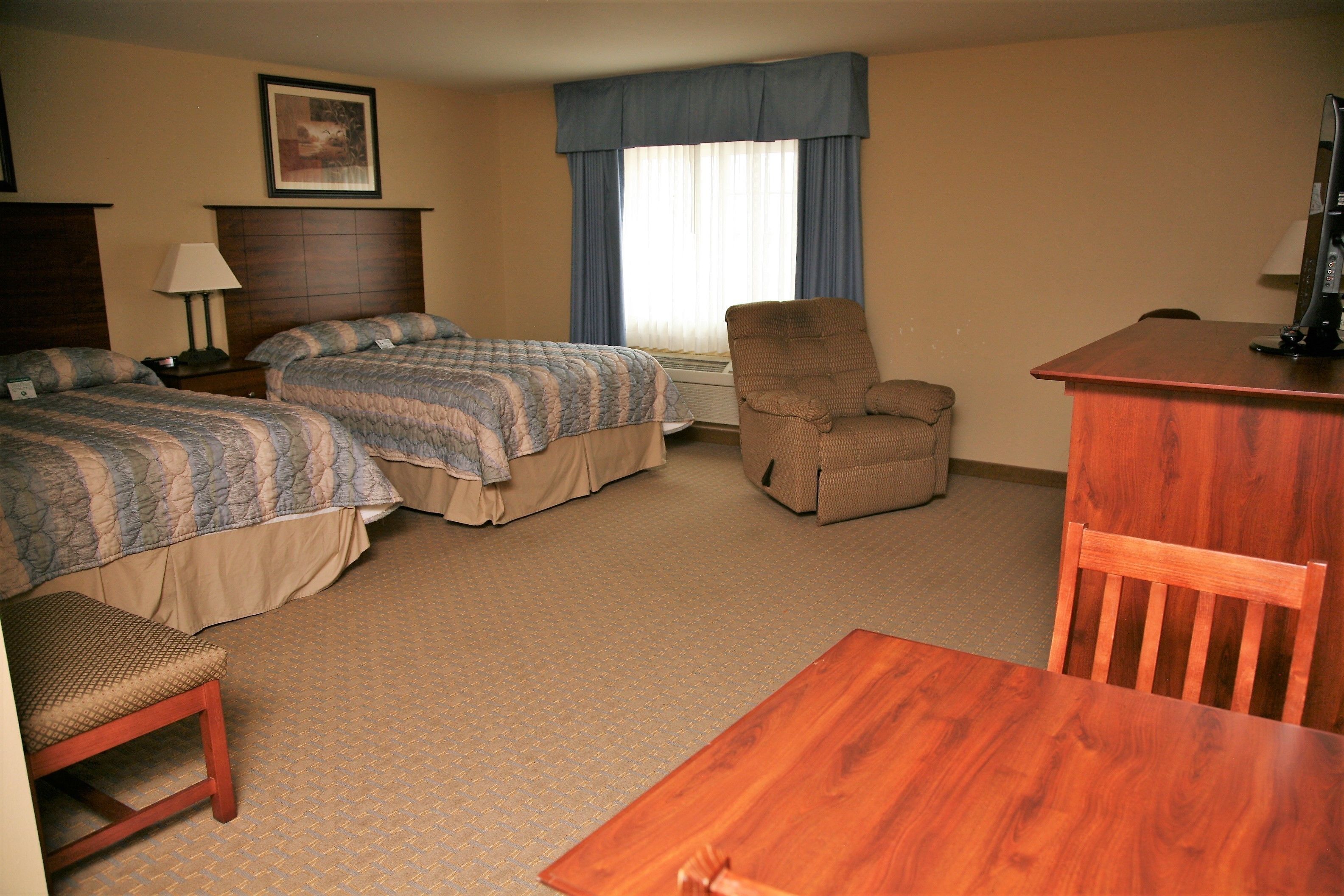 A hotel room with two beds, a desk, a chair, and a small table.