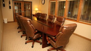 A conference room with a large wooden table, six brown leather chairs, a clock on the wall, and a window with blinds.