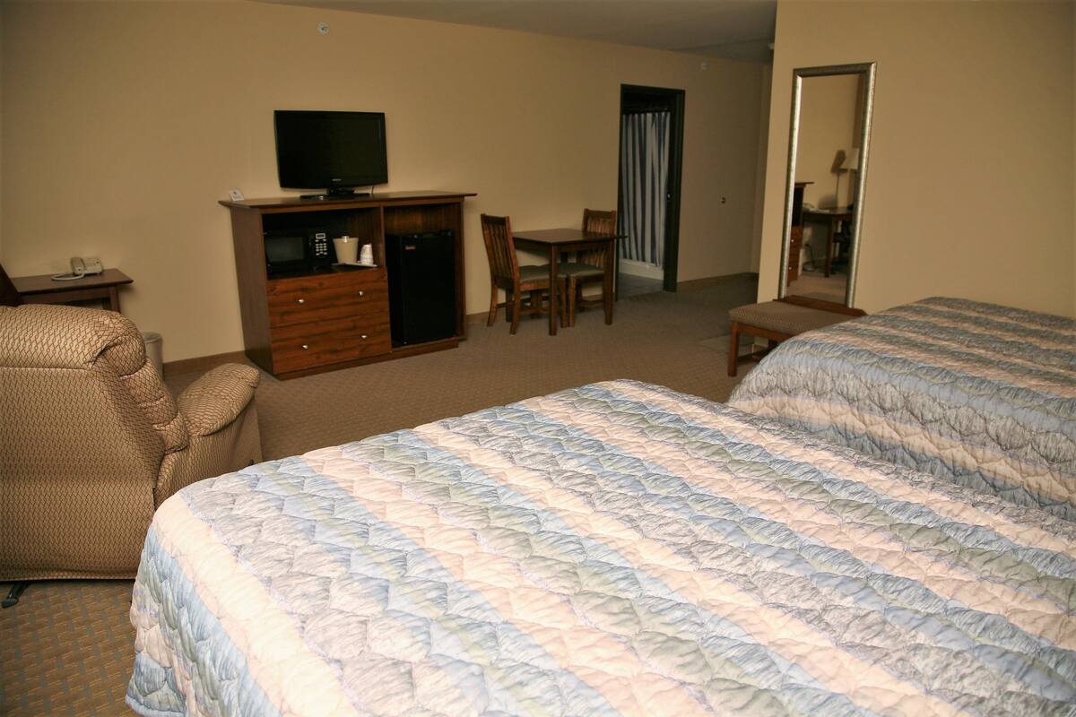 A hotel room with two beds, a TV, a desk with a chair, a wardrobe, and a mirror.