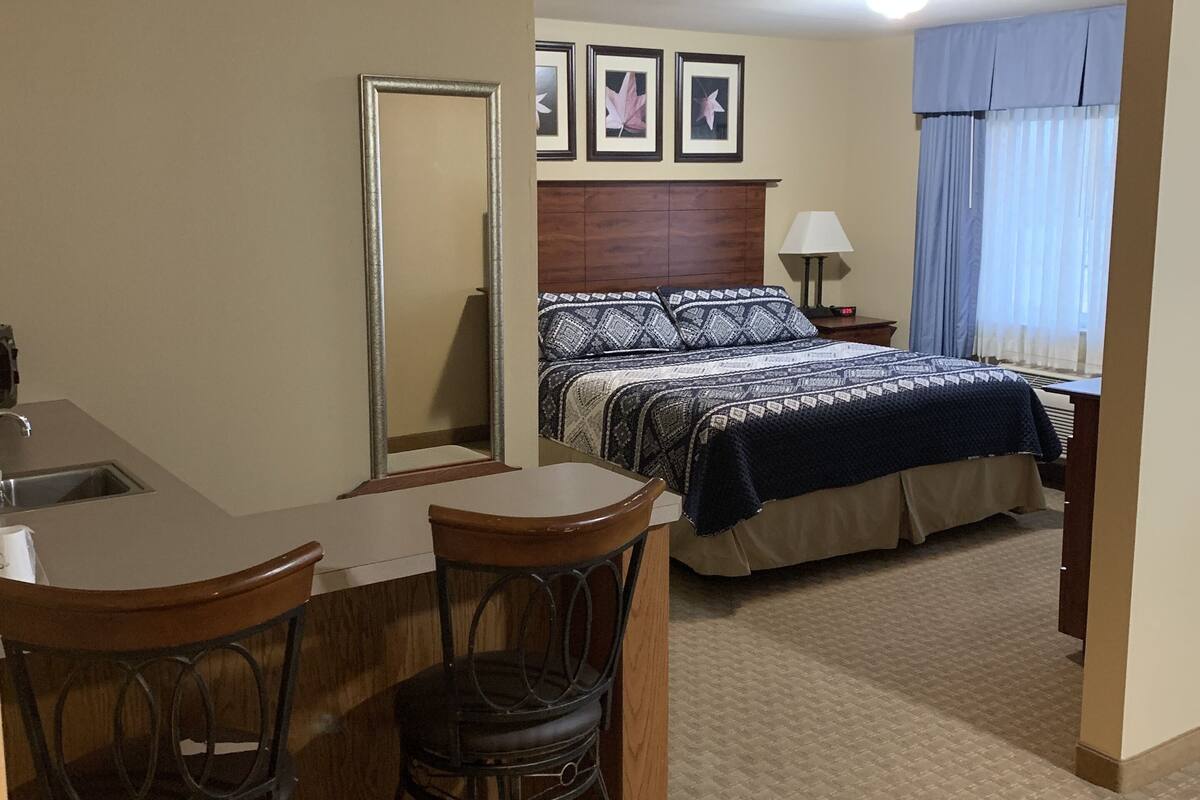A hotel room with a bed, a desk with two chairs, a mirror, and a nightstand with a lamp.
