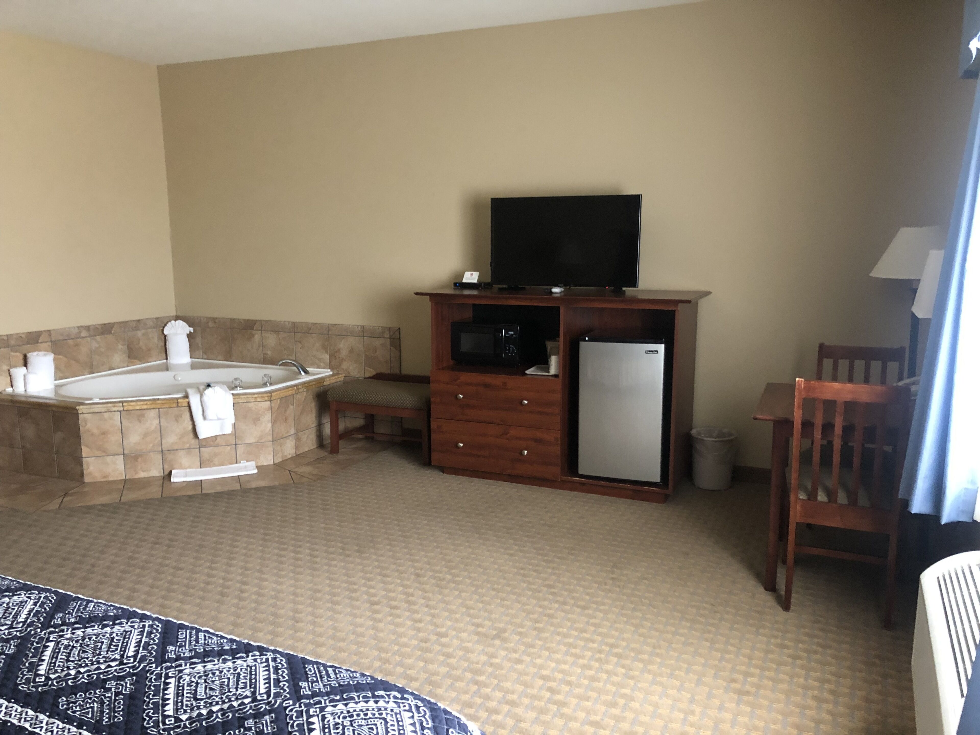 A hotel room with a large bathtub, a small refrigerator, a television on a wooden cabinet, and a wooden chair.