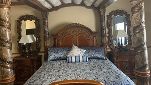 A four-poster bed with a patterned bedspread and pillows, flanked by ornate wooden furniture and mirrors.