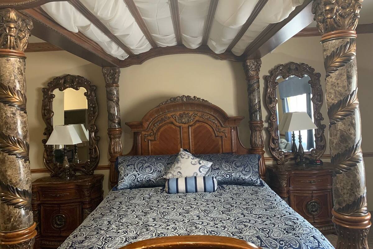 A four-poster bed with a patterned bedspread and pillows, flanked by ornate wooden furniture and mirrors.