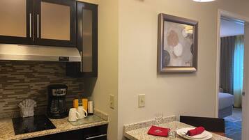 A hotel kitchen with a coffee maker, a framed artwork, and a fire alarm.
