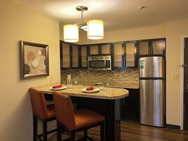 A modern kitchen with granite countertops, stainless steel appliances, and a dining area with a chair and table.