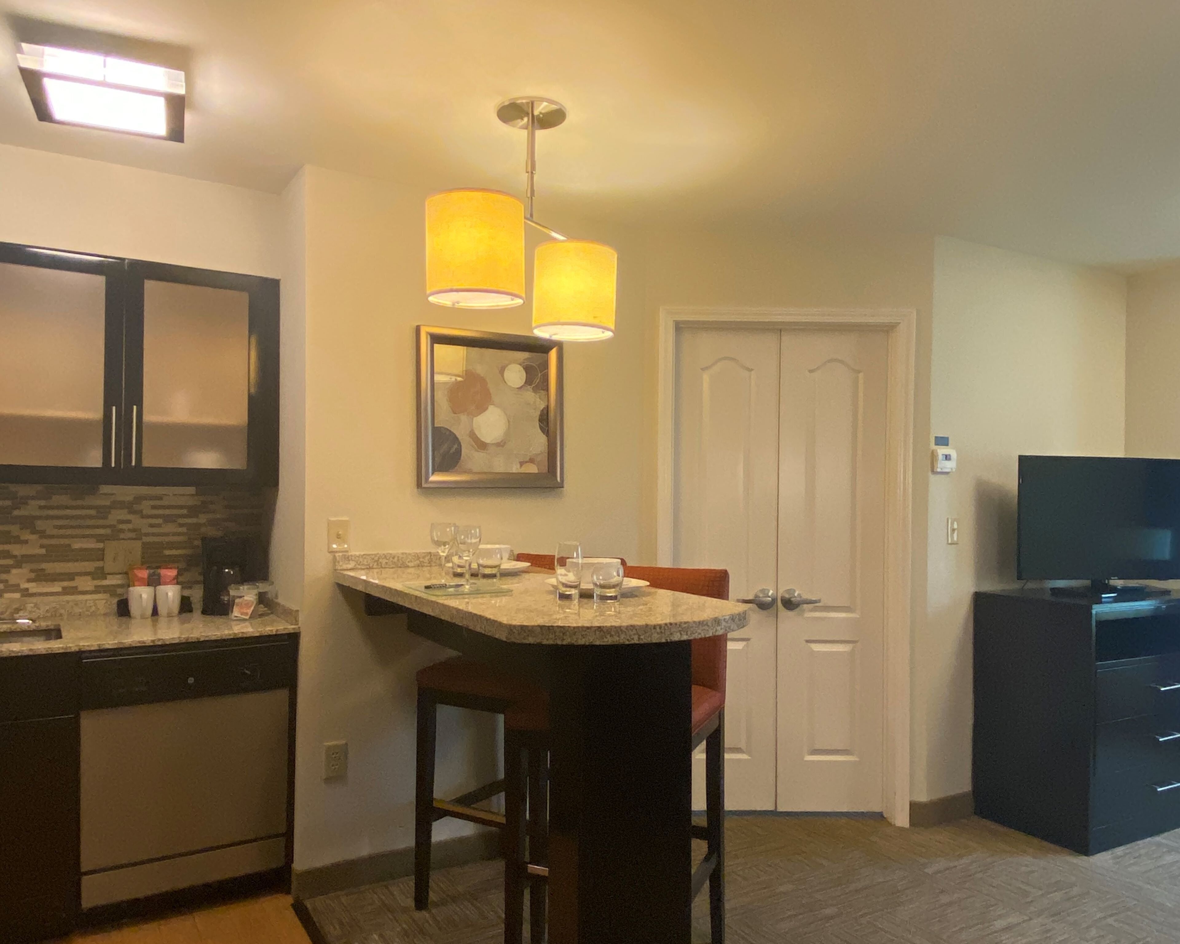 A compact kitchen with a bar area, a dining table, and a television.
