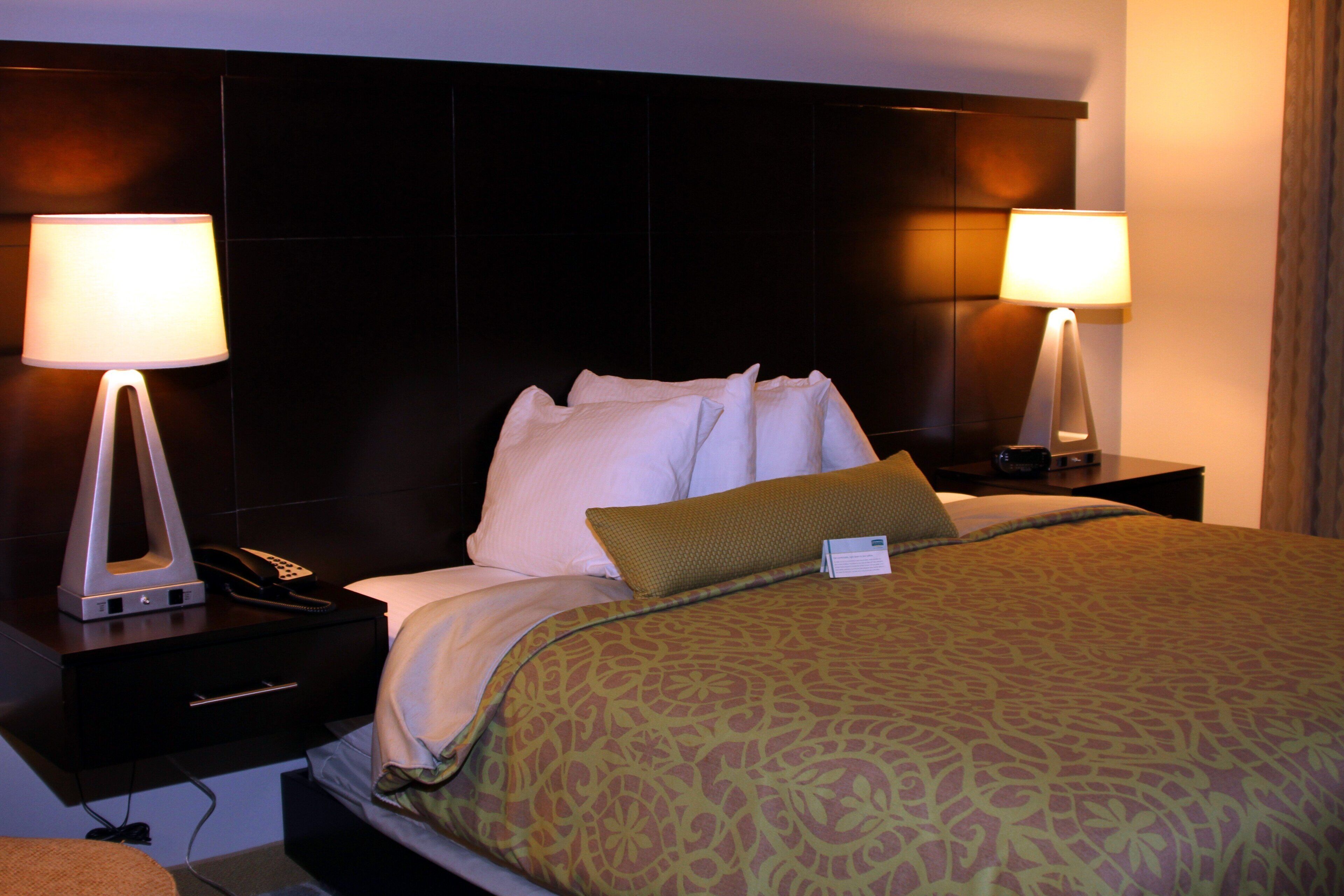 A hotel room with a bed, two bedside lamps, a telephone, and a nightstand.