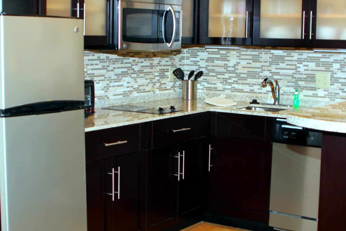 A modern kitchen with dark cabinets, a stainless steel refrigerator, a microwave, and a dishwasher.