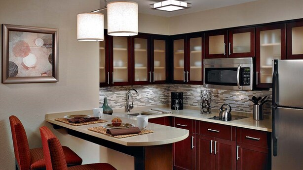 A modern kitchen with dark wooden cabinets, stainless steel appliances, and a central island with seating. - Staybridge Suites Liverpool Syracuse by IHG (Liverpool)