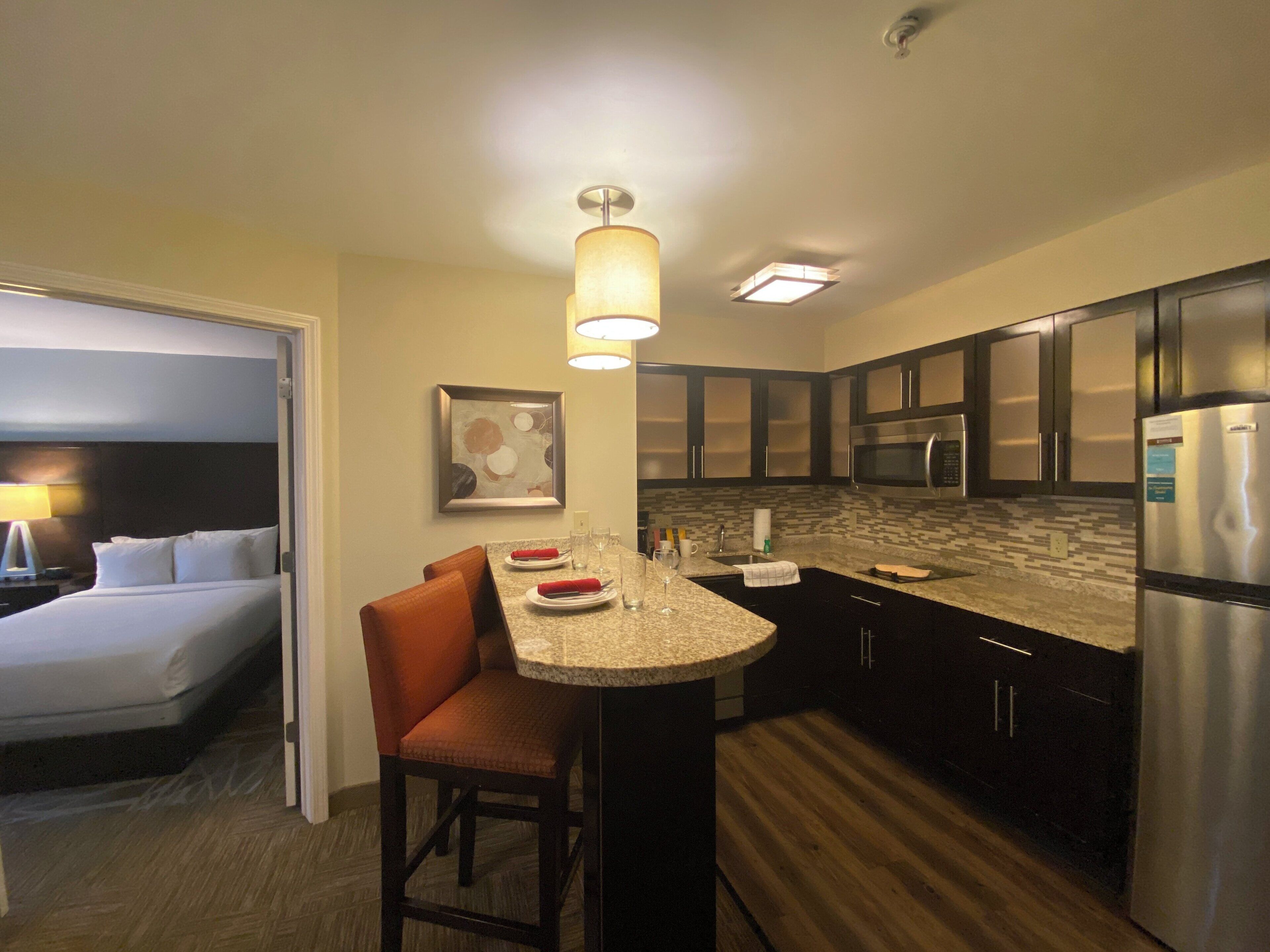 A hotel room with a kitchenette, a bed, and a dining area.
