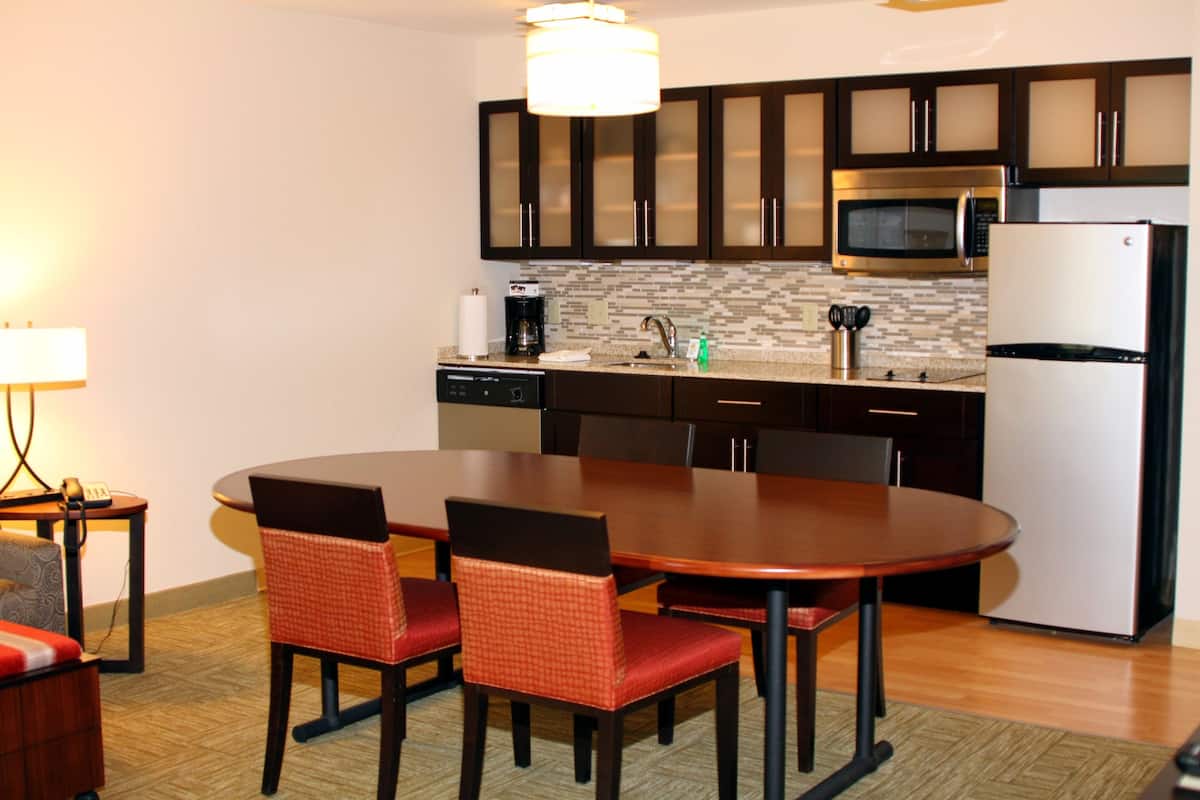 A modern kitchen with dark cabinets, a stainless steel microwave, a built-in oven, and a refrigerator. There is a dining table with four chairs.