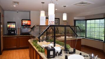 A buffet area with a Coca-Cola refrigerator, a coffee machine, and a variety of food items.
