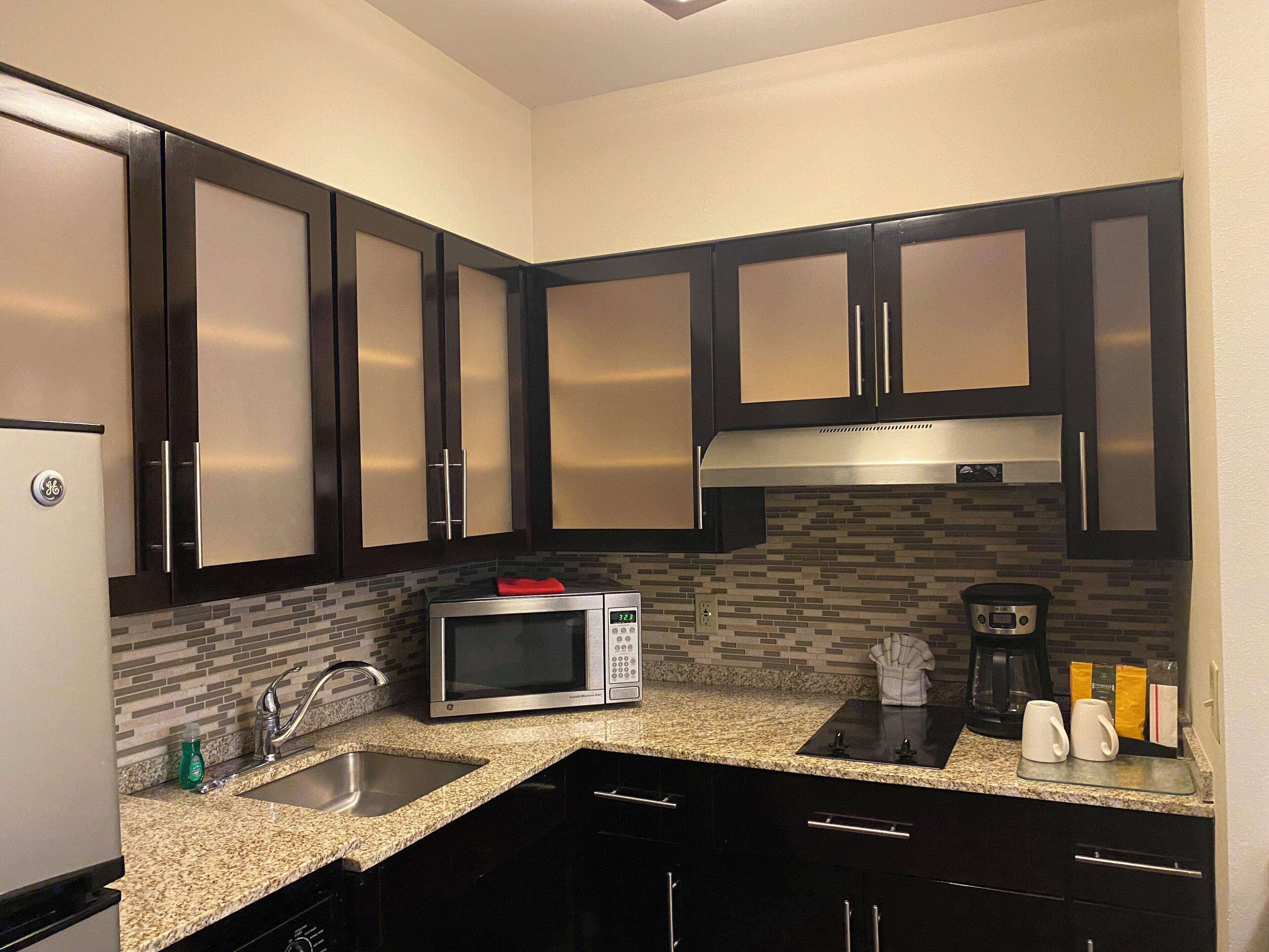 A kitchen with dark cabinets, a stainless steel microwave, a coffee maker, and a sink.