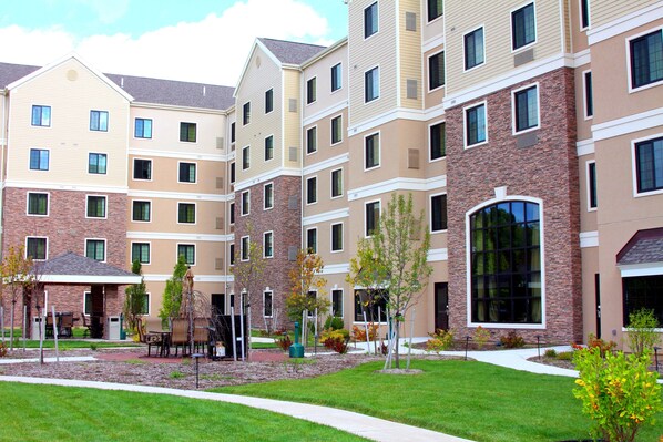 A multi-story hotel with a brick facade, multiple windows, and a landscaped courtyard with outdoor seating.
