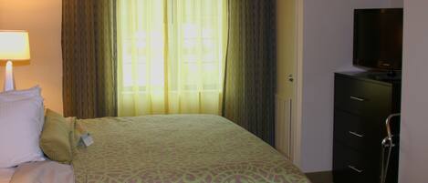 A hotel room with a bed, a TV on a dresser, and a window with curtains.