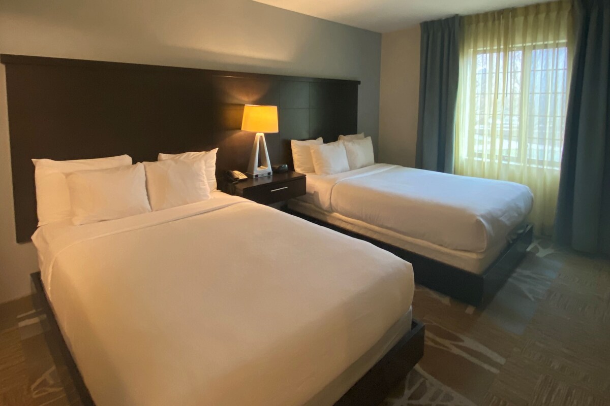 Une chambre d’hôtel avec deux lits, une table de chevet avec une lampe et une fenêtre avec des rideaux.