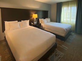 A hotel room with two beds, a nightstand with a lamp, and a window with curtains.