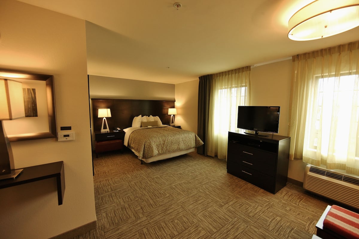 A hotel room with a bed, a TV, a desk, and a window with curtains.