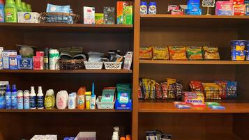 Uma loja bem organizada com prateleiras repletas de produtos domésticos e de higiene pessoal, incluindo produtos de limpeza, artigos de toilette e lanches.