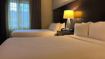 Une chambre d’hôtel avec deux lits, une table de chevet avec une lampe et une fenêtre avec des rideaux.