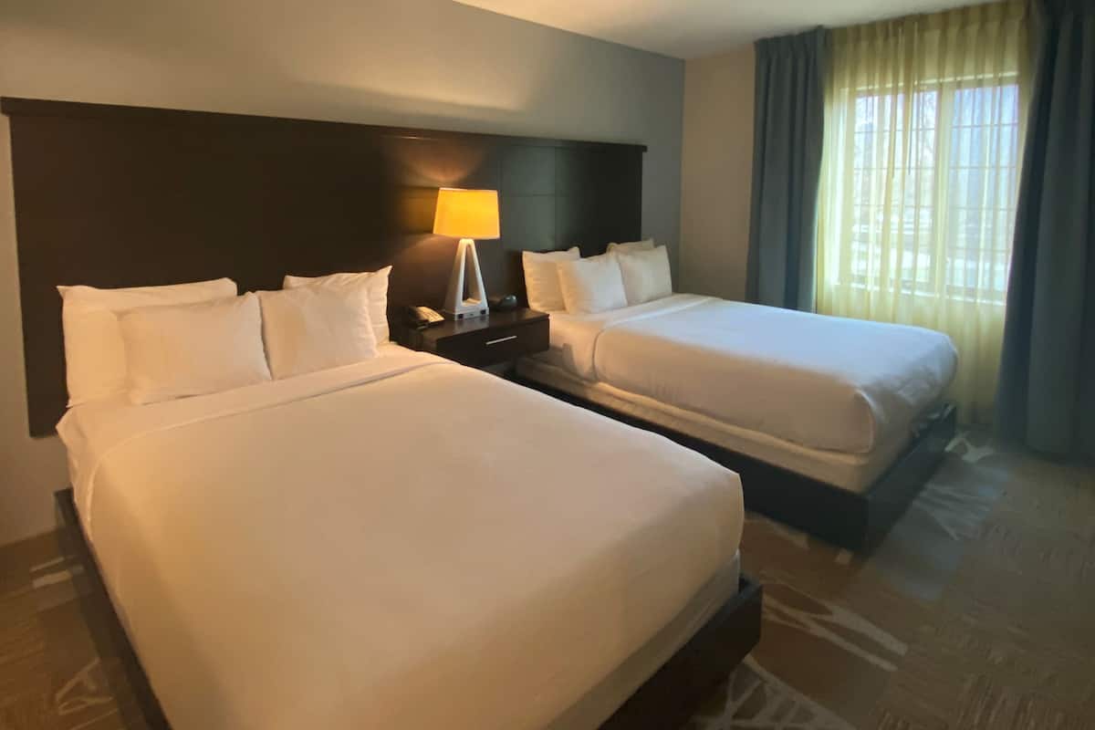 A hotel room with two beds, a nightstand with a lamp, and a window with curtains.