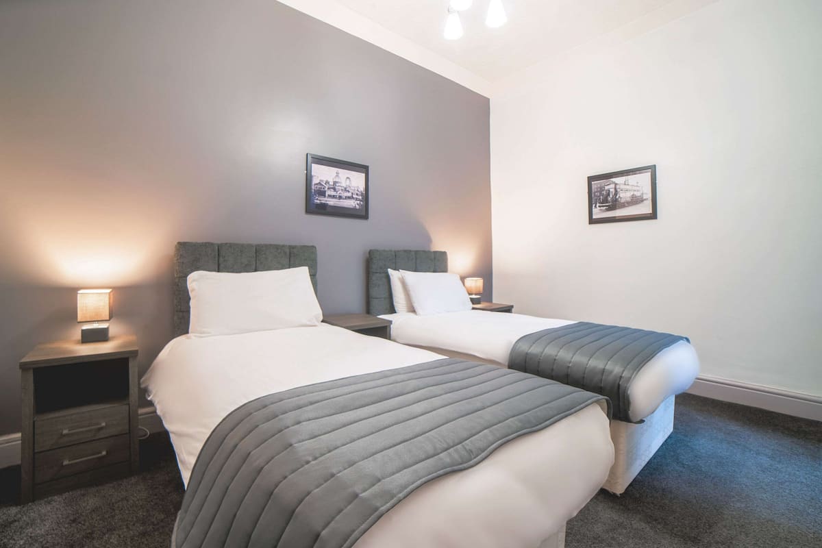 Une chambre d’hôtel avec deux lits, chacun doté d’une tête de lit, de tables de chevet avec des lampes et de tableaux encadrés accrochés au mur.
