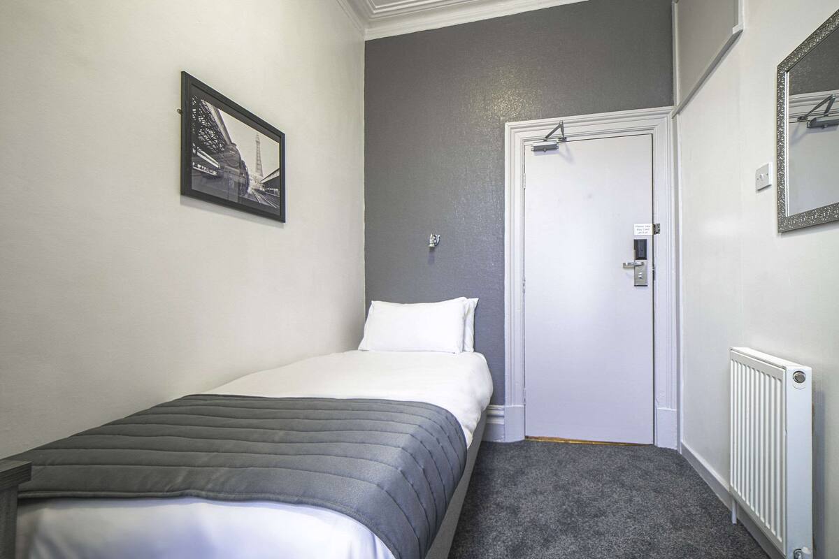 Une chambre à coucher avec un lit, une porte, un radiateur et un tableau encadré au mur.